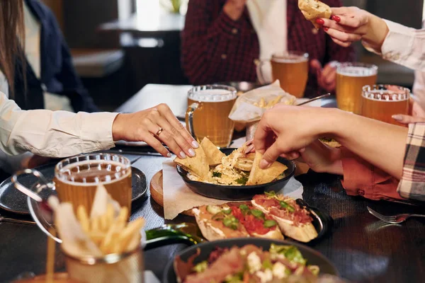 Delicious food. Group of young friends sitting together in bar with beer.