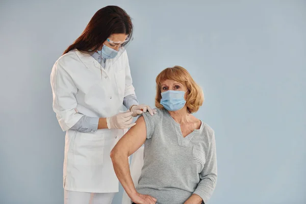 Young female doctor giving injection to senior woman at hospital.