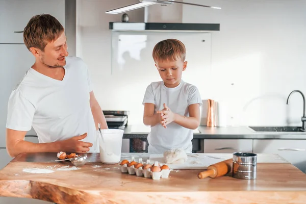 Eggs, milk and dough. Father teaching his little son with preparing of sweet christmas cookies.