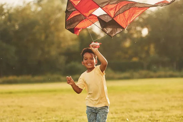 赤い凧で走る アフリカ系アメリカ人の子供は夏の昼間にフィールドで楽しんでいます — ストック写真