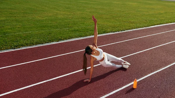 Woman is on the running track exercising outdoors.