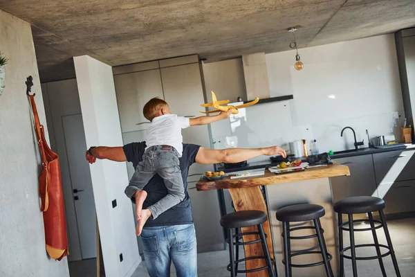 Playing with yellow toy plane. Father and son is indoors at home together.