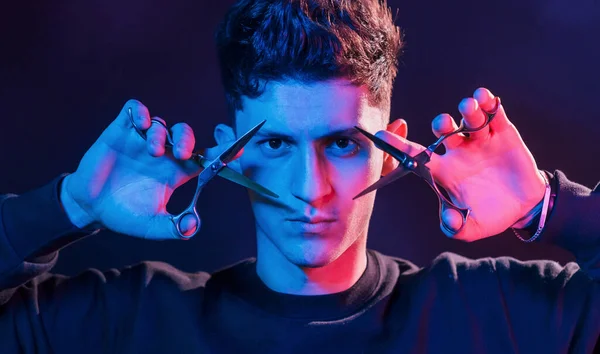 Trzyma Nożyczki Młody Fryzjer Sprzętem Roboczym Stojący Studio Oświetleniem Neonowym — Zdjęcie stockowe