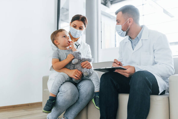 С маленьким мальчиком, которого осматривают. Два врача в белых халатах работают вместе в клинике..