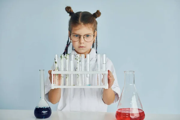 Works with test tubes. Little girl in coat playing a scientist in lab by using equipment.