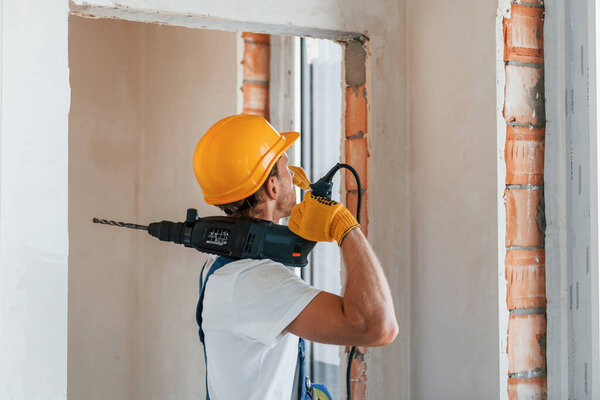 Empty walls. Young man working in uniform at construction at daytime.