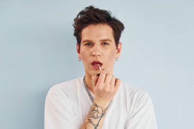Genç eşcinsel adam stüdyoda duruyor ve kameraya poz veriyor. Kırmızı renkli dudaklar..