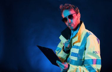 Polis üniformasıyla. Neon ışıkları. Genç Avrupalı adam karanlık stüdyoda..