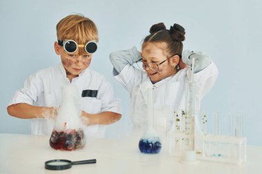 Kız ve erkek birlikte çalışıyorlar. Beyaz önlüklü çocuklar laboratuarda ekipman kullanarak bilim adamlarını oynuyorlar..