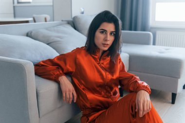 Kırmızı kostümlü bir kamera için poz vermek. Genç kadın, gündüz vakti modern evin içinde..