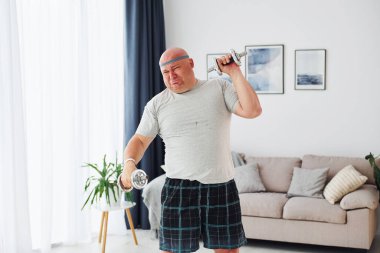 Dambıl kullanıyor. Sıradan giysili komik şişman adam evde..