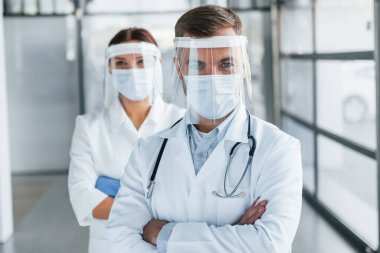 Kollarını kavuşturmuş duruyorsun. Beyaz önlüklü iki doktor klinikte birlikte çalışıyorlar..