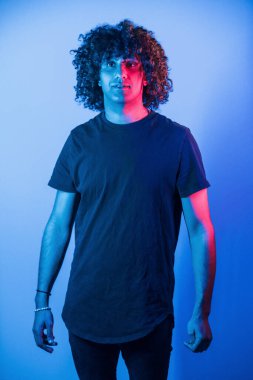 Kamera için poz vermek. Kıvırcık saçlı genç adam stüdyoda neon ışıklı..