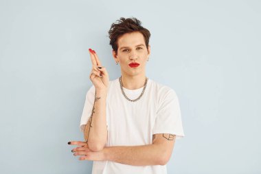 Genç eşcinsel adam stüdyoda duruyor ve kameraya poz veriyor. Dudaklar kırmızı rujla.