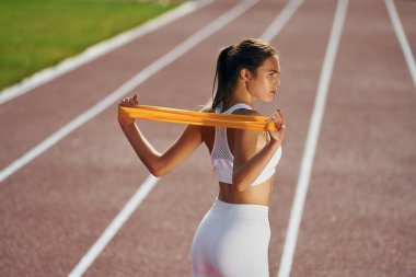 Bant kullanarak esneme hareketleri yapıyor. Spor elbiseli genç bayan dışarıda egzersiz yapıyor..
