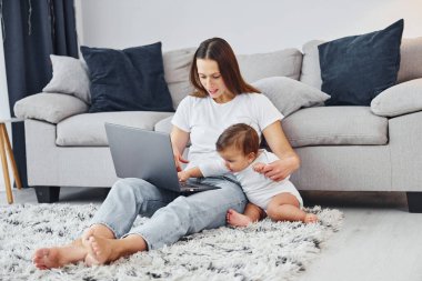 Gümüş renkli laptop. Anne ve küçük kızı evde birlikte..