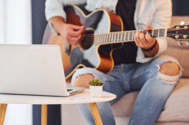 Şarkı yapıyorum. Gündelik giysiler içinde ve akustik gitarlı bir adam içeride..