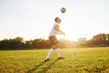 Arka planda orman var. Genç futbolcu spor sahasında antrenman yapıyor..