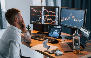 Alkolle. Resmi giyinmiş genç işadamı birden fazla ekranla ofiste..