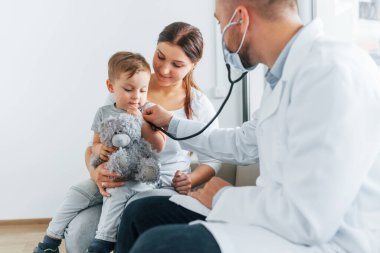 Küçük çocuk inceleniyor. Beyaz önlüklü iki doktor klinikte birlikte çalışıyorlar..