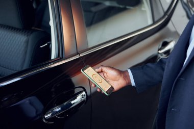 Kapıyı açmak için akıllı telefonu kullanmak. Siyah takım elbiseli genç Afro-Amerikan iş adamı Ototalon..