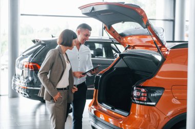 Modern araç. Resmi kıyafetli adam, müşteriye otomobil seçiminde yardımcı oluyor..