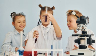 Renkli sıvıyla test tüpleri. Beyaz önlüklü çocuklar laboratuarda ekipman kullanarak bilim adamlarını oynuyorlar..