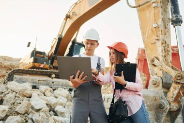 Laptop kullanıyorum. Gündüz vakti iki işçi ödünç alma çukurunda beraberler..