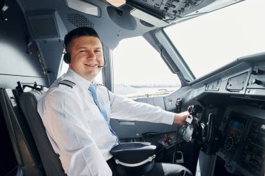 Yan görüş. Resmi kıyafetli pilot kokpitte oturur ve uçağı kontrol eder..