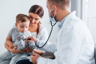 Çocuğa yardım ediyorum. Beyaz önlüklü iki doktor klinikte birlikte çalışıyorlar..
