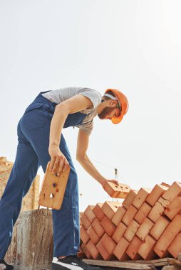 Tuğla taşıyorum. Üniformalı genç inşaat işçisi tamamlanmamış binada meşgul..
