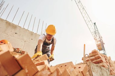 Tuğla kullanarak. Üniformalı genç inşaat işçisi tamamlanmamış binada meşgul..