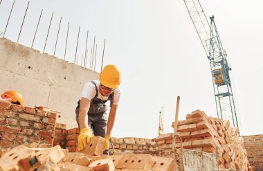 Tuğla kullanarak. Üniformalı genç inşaat işçisi tamamlanmamış binada meşgul..