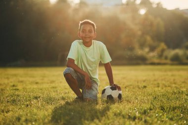 Mola verdim. Futbol topuyla. Afrikalı Amerikalı çocuk yaz günlerinde tarlada eğleniyor..