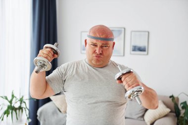 Dambıl kullanıyor. Sıradan giysili komik şişman adam evde..