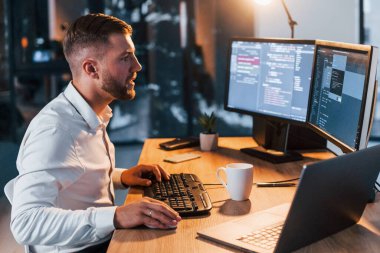 Gece vakti. Resmi giyinmiş genç işadamı birden fazla ekranla ofiste..