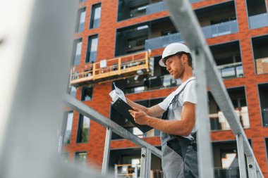 Proje yöneticisi. Gündüz vakti inşaatta üniformalı genç bir adam çalışıyor..