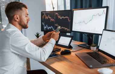 Grafikler ve diyagramlar. Resmi giyinmiş genç işadamı birden fazla ekranla ofiste..