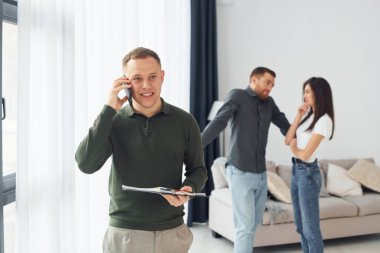 Satıcı, genç bir çiftin daire seçmesine yardım ediyor. İş ve kira kavramı.