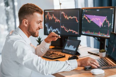 Laptop kullanıyorum. Resmi giyinmiş genç işadamı birden fazla ekranla ofiste..