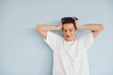 Genç eşcinsel adam stüdyoda duruyor ve kameraya poz veriyor. Sıradan beyaz gömlekli..