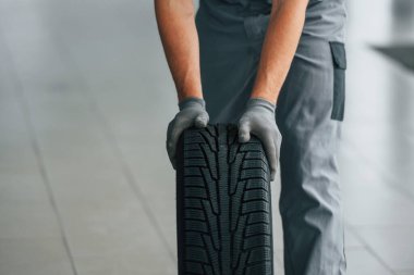 Lastik yerde. Üniformalı adam gündüz vakti otosalonda çalışıyor..