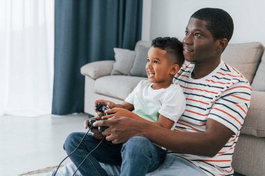 Oyun oynamak için joystickleri kullanmak. Afrikalı Amerikalı baba ve küçük oğlu evde..
