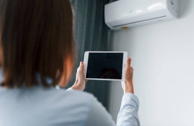 Klimayı tabletle kontrol etmek. Genç kadın, gündüz vakti modern evin içinde..