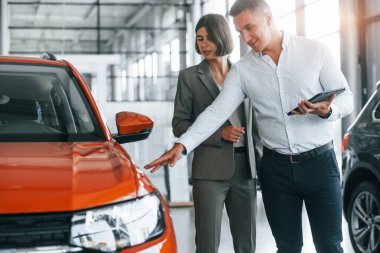 Modern araçlar. Resmi kıyafetli adam, müşteriye otomobil seçiminde yardımcı oluyor..