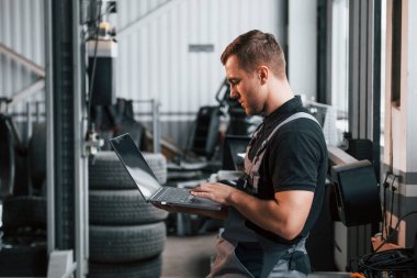 Dizüstü bilgisayarı elinde tutuyor. Üniformalı adam otomobil servisinde çalışıyor..