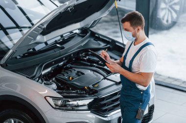 Kaput açıldı. Beyaz gömlekli ve mavi üniformalı genç adam otomobil tamir ediyor..