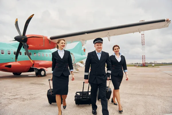 With luggage. Aircraft crew in work uniform is together outdoors near plane.