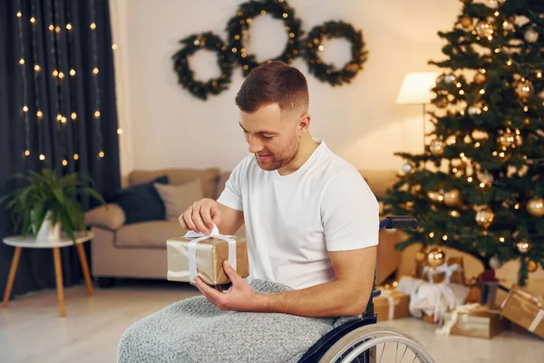 Unboxing preset. New year is coming. Disabled man in wheelchair is at home.