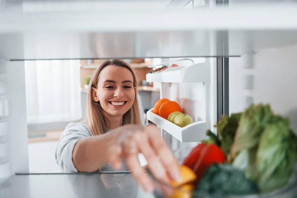 Happy woman taking vegetable from the fridge.